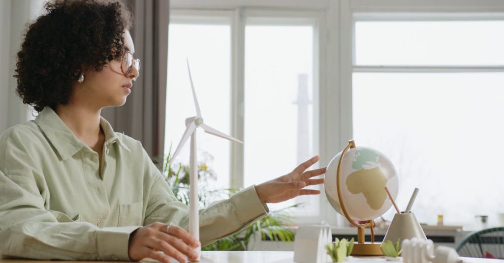 A young woman explores renewable energy with a globe and wind turbine model indoors.